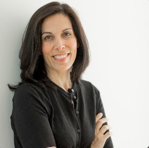Woman with shoulder-length dark hair wearing a black long-sleeve shirt stands against a white background, smiling with arms crossed.